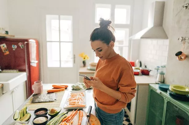 Photo of a Young Woman checking sushi recipes online in the kitchen of her apartment.