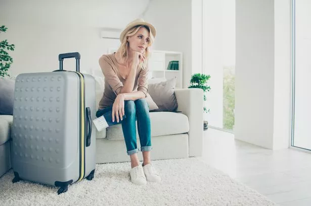 Full legs body size exhausted ponder think pensive curly wavy lady in her casual clothes denim jeans shoes she hold boarding pass sit on cozy comfort couch sofa in modern light house wait taxi