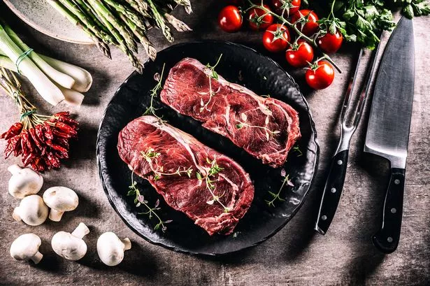 Two Beautiful Raw Beef Steaks on a Black Plate, Mushrooms, Asparagus Onion Tomatoes and Chili Peppers Top of View.