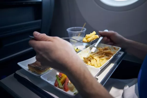 Passenger Eating Airline Meal With Metal Cutlery. Menu With Pasta, Vegetable, Dessert and Drink on Tray During Long Haul Flight.