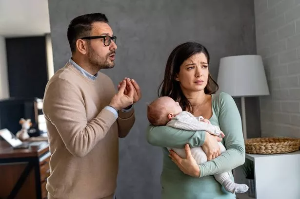 Young unhappy father with baby and wife suffering from postnatal depression at home.