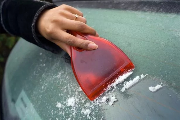 A Young Woman Scraping Ice From A Frozen Car Windscreen with a Red Ice Scraper