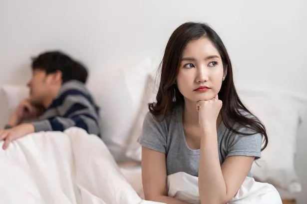 Woman Looking Pensitive With Her Husband in the Background while they have in Bed