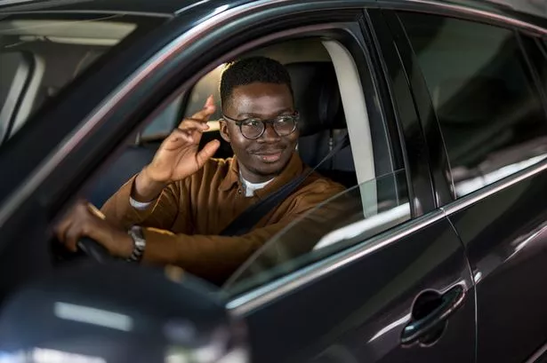 Smiling African American Businessman Driving His Car and Waving.