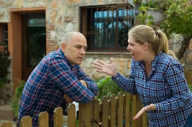 Neighbors standing on either side of fence and arguing (stock photo)