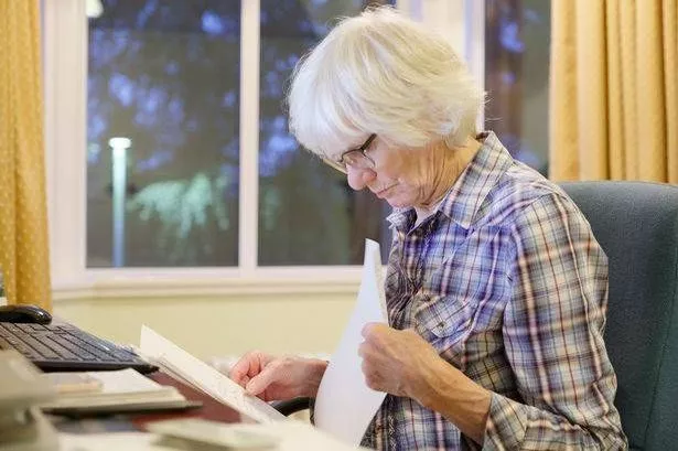 Older Woman is Looking at Paperwork Seated at a Desk