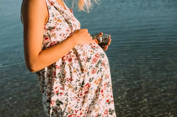 Pregnant Woman with White Hair on the Beach in a Dress and Sunglasses at Sunset