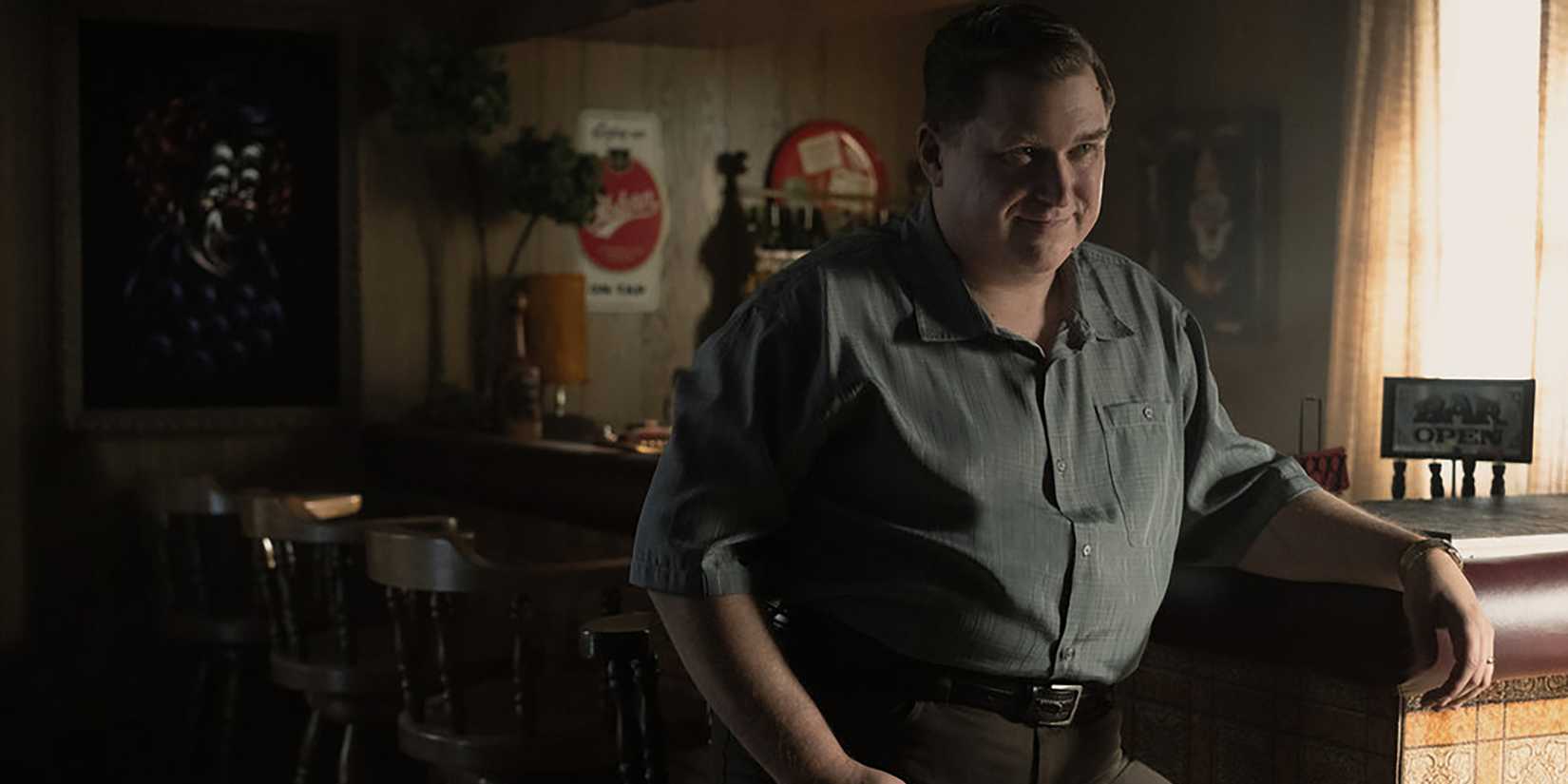 Michael Chernus as John Wayne Gacy sitting at a bar and smiling creepily in Devil in Disguise: John Wayne Gacy