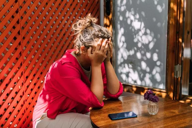 A woman in a pink blouse sits on the street cafe in sunny day and she is sad, depression concept. Phone on the table.