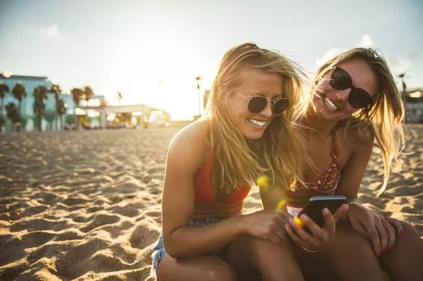 Two girls browsing the net while sitting on the beach.
