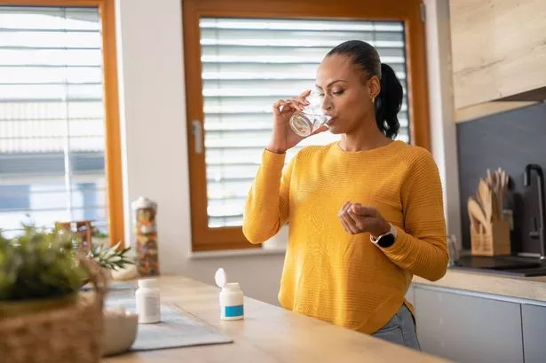Young woman taking medicine, vitamin with water at home. Modern lifestyle and healthcare concept.