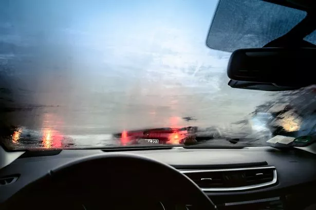 inside of a car windshield, which is misty. the brake lights of other vehicles are visible, but blurred