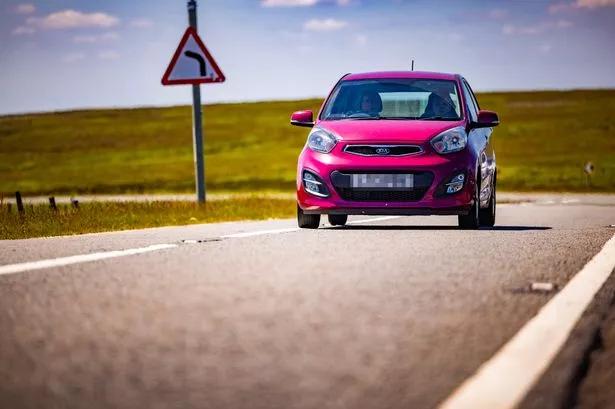 a red car drives on a road with green hills in the background