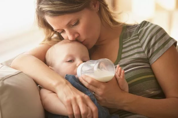 Young mother cradles a baby in her arms, kisses its forehead and feeds the child a bottle full of milk